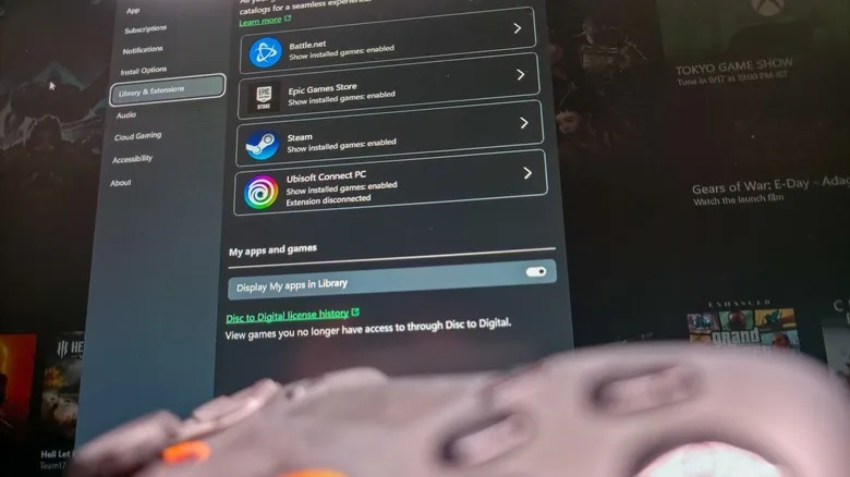 Mando desenfocado en primer plano con las integraciones de biblioteca de la aplicación Xbox al fondo