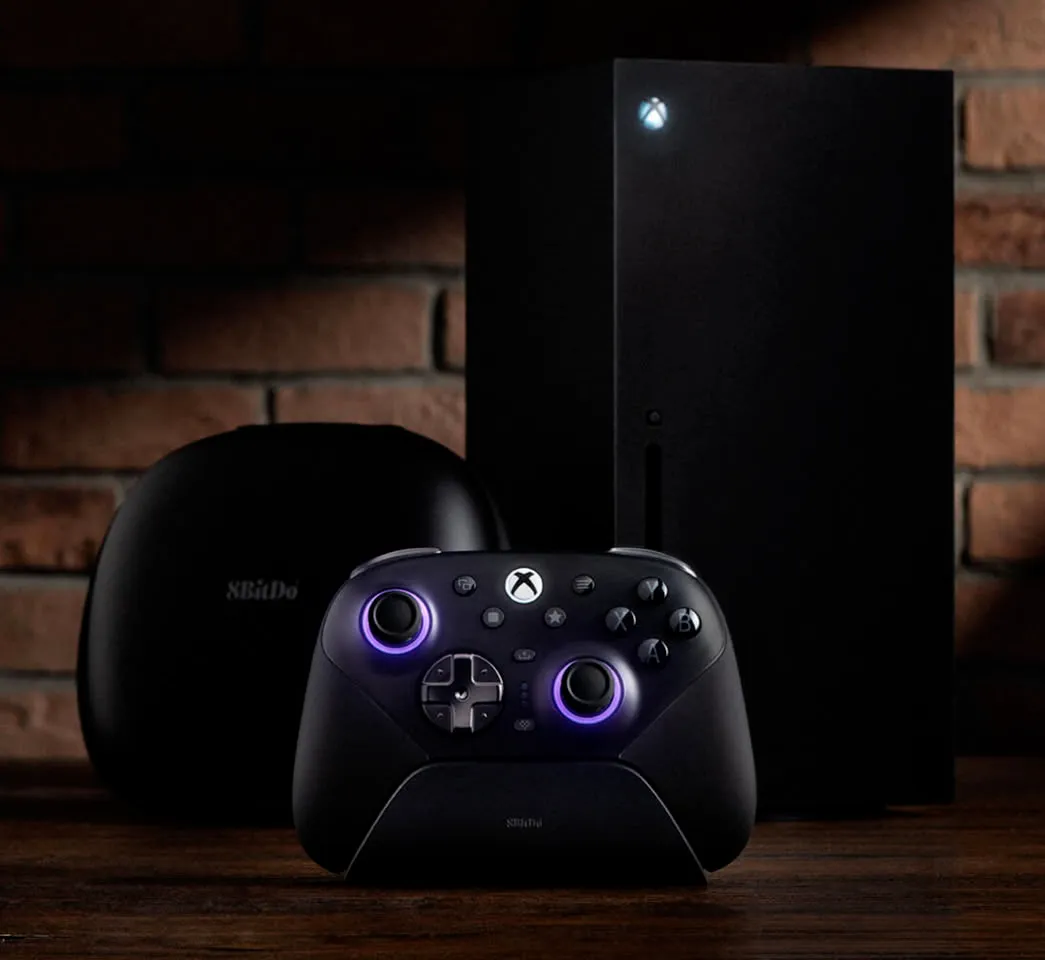 8BitDo Ultimate 3E en su base de carga junto a una Xbox Series X y el estuche de transporte