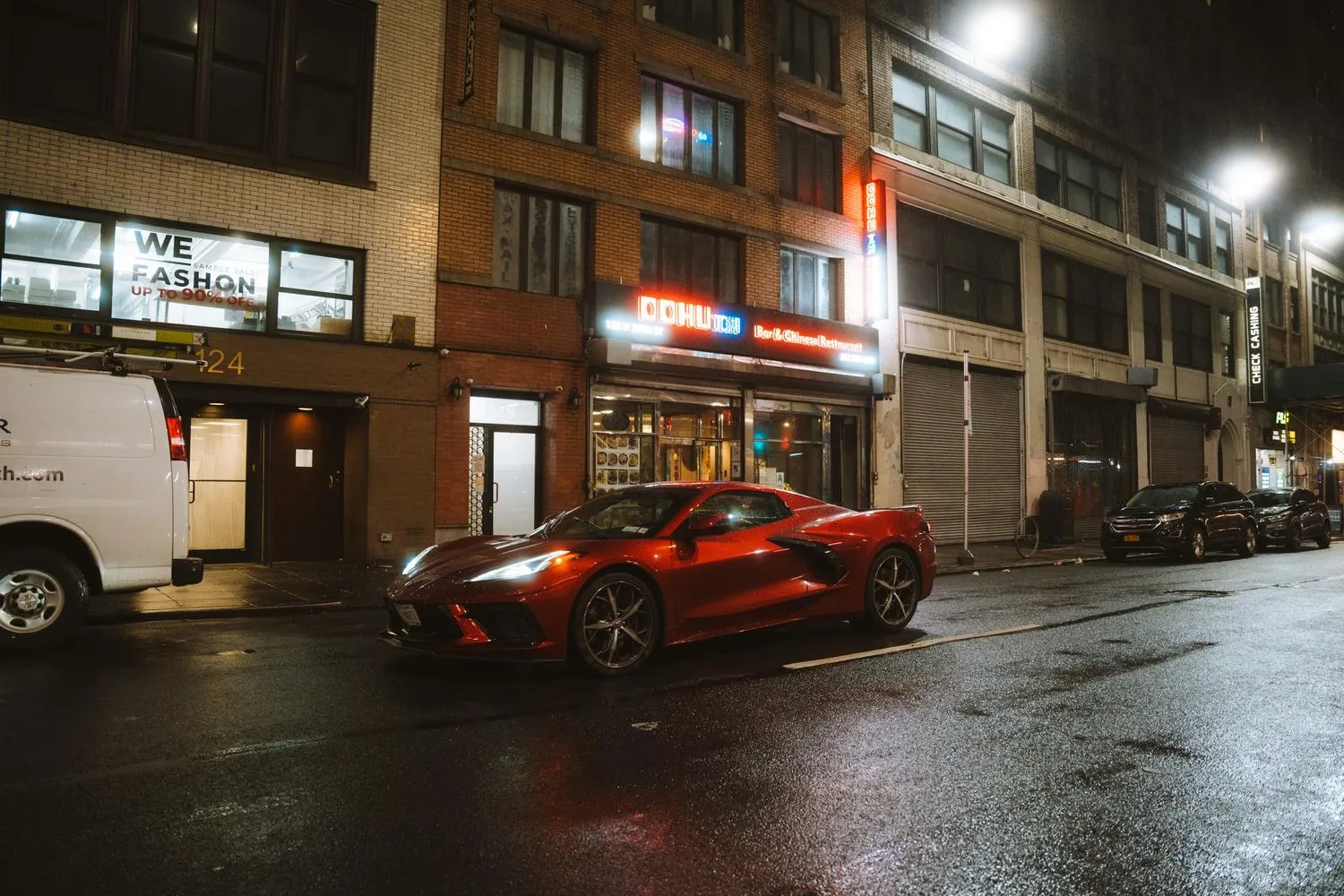 Coche deportivo rojo aparcado en una calle de ciudad nocturna iluminada con luces de neón