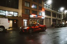 Coche deportivo rojo aparcado en una calle de ciudad nocturna iluminada con luces de neón