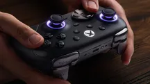 Hands holding the black 8BitDo Ultimate 3E with the joystick rings lit in violet