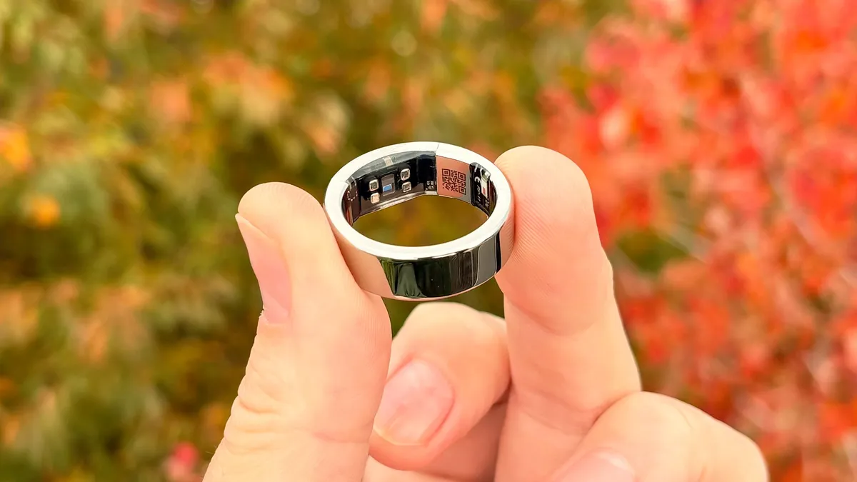 Ultrahuman Ring Pro plateado sostenido entre dos dedos, con sus sensores interiores visibles