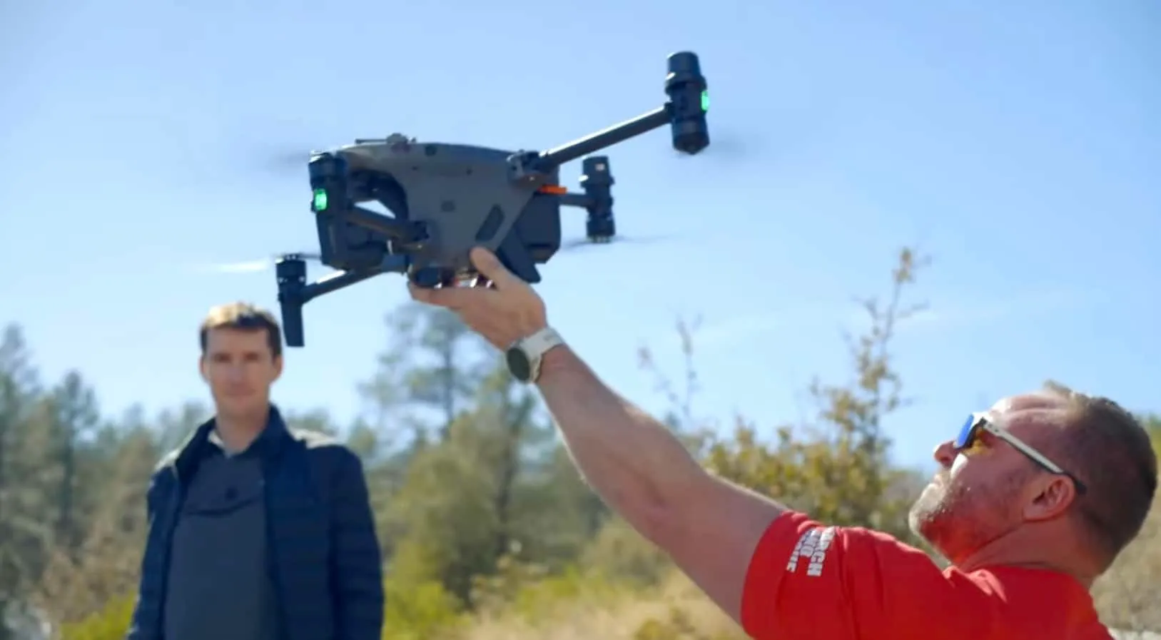 Captain Kyle Nordfors, in a red Weber County Search and Rescue shirt, holds a DJI Matrice 30T aloft as he hand-launches it under a blue sky