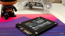 Un SSD SATA junto a un teclado y un mando de consola sobre una alfombrilla