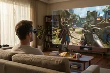 Persona sentada en un sofá con gafas AR mientras ve una pantalla virtual grande con un videojuego