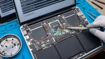 MacBook Air M5 abierto sobre una mesa de reparación, con la placa base a la vista y signos de corrosión