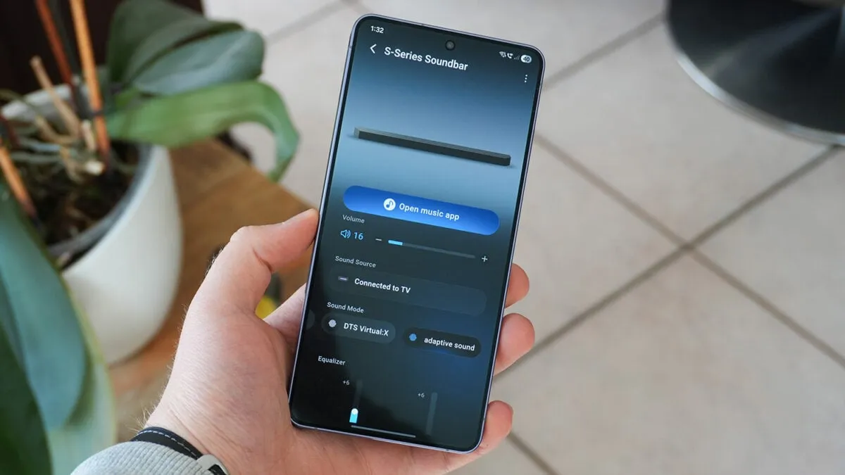 A hand holding a Samsung phone running the Samsung Sound app to control an S-Series soundbar