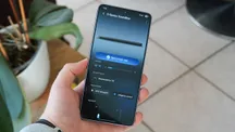 A hand holding a Samsung phone running the Samsung Sound app to control an S-Series soundbar