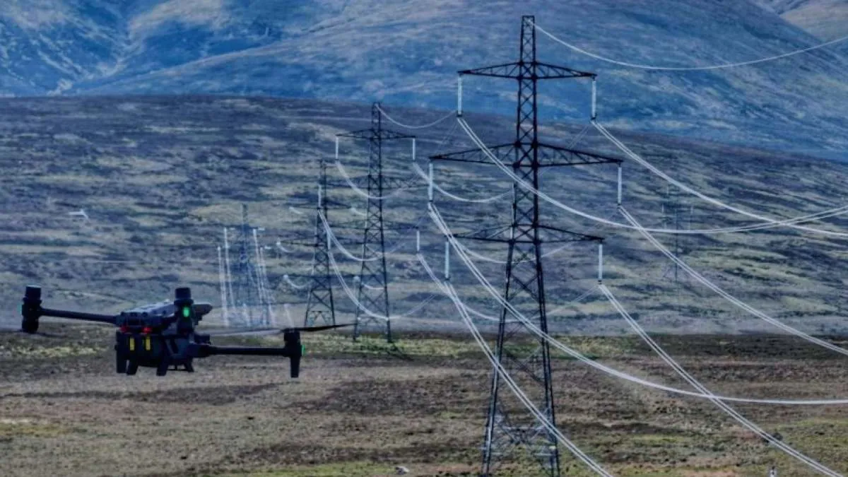 Inspection drone in the foreground flying over moorland, with several high-voltage towers and their power lines stretching across the valley