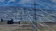 Inspection drone in the foreground flying over moorland, with several high-voltage towers and their power lines stretching across the valley
