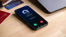 Un teléfono negro sobre una mesa de madera recibe una llamada de un número desconocido