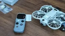 Dron DJI Neo 3 blanco con hélices protegidas por jaulas junto al mando DJI RC Mini con pantalla sobre una mesa de madera