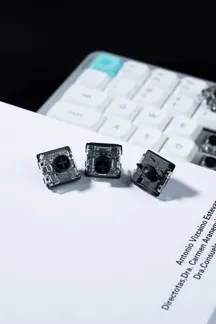Tres interruptores de perfil bajo Gateron en primer plano sobre un documento, con un teclado al fondo