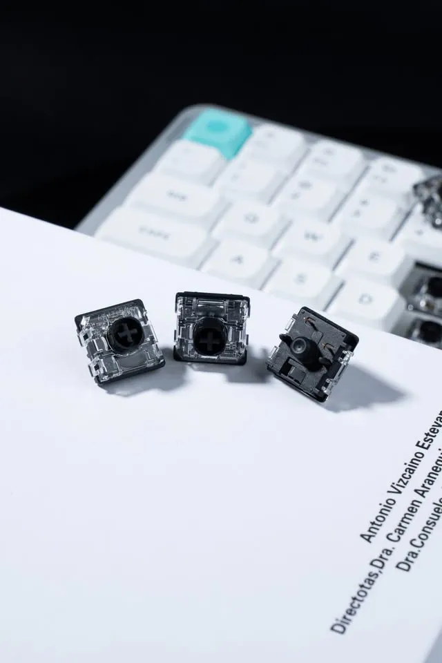 Tres interruptores de perfil bajo Gateron en primer plano sobre un documento, con un teclado al fondo