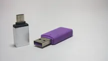 Dos adaptadores de USB-A a USB-C, uno plateado y otro morado, apoyados sobre una superficie