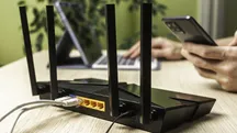 Mano que sostiene un teléfono junto a un router inalámbrico con cables conectados