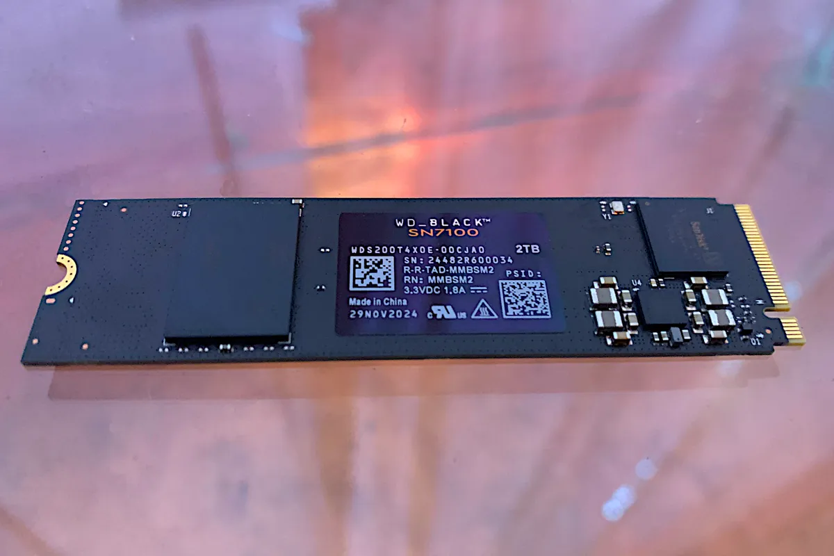 Unidad SSD WD Black SN7100 junto a su embalaje, de frente sobre fondo claro