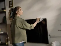 Person cleaning the screen of a flat-screen TV in a living room with a white cloth