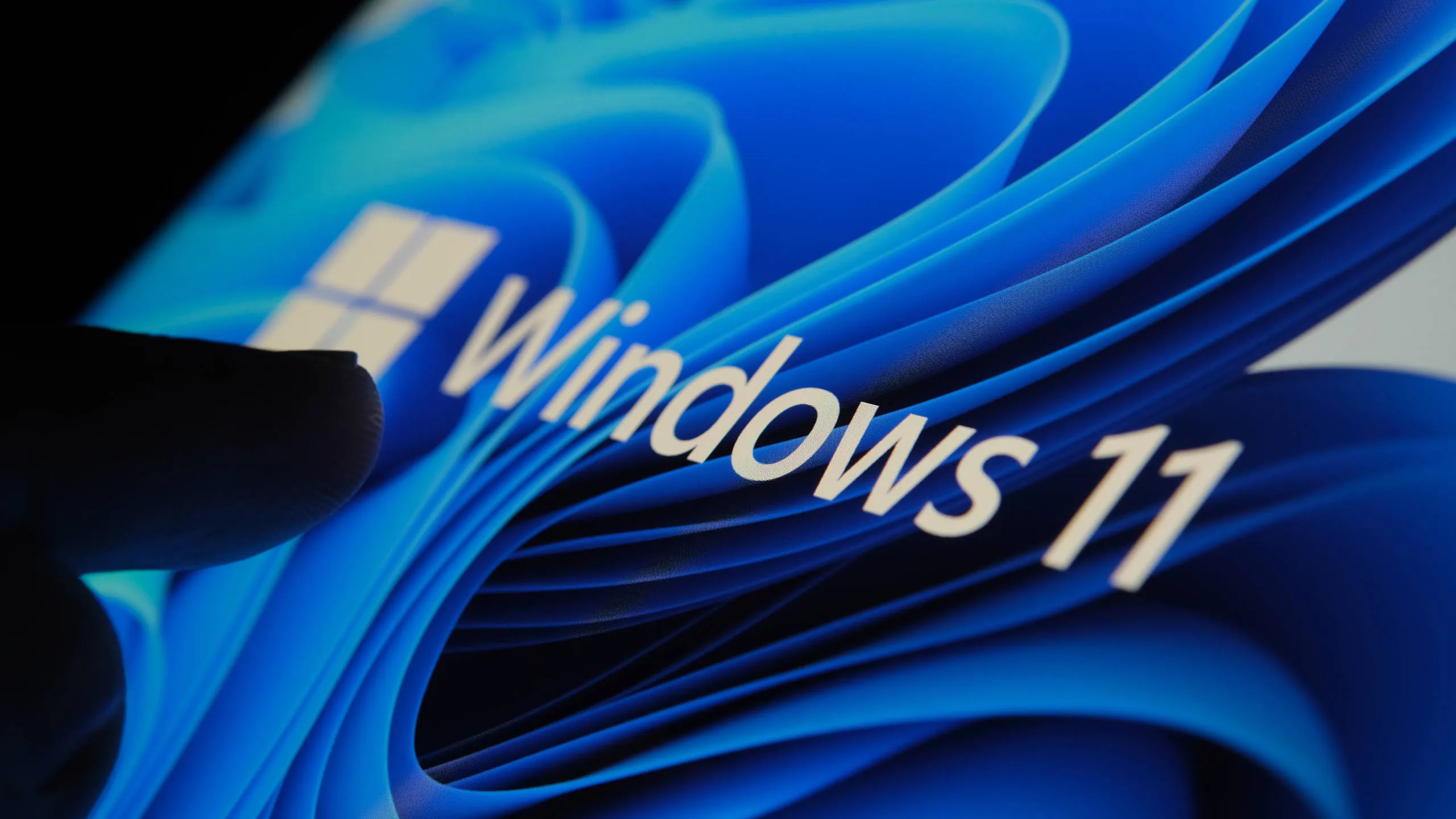 Dedo tocando el logotipo de Windows 11 en una pantalla a oscuras