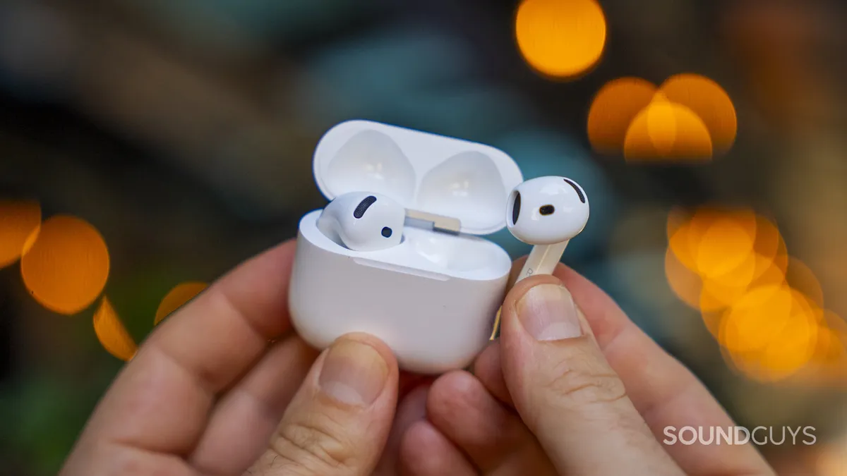 Un AirPod sujeto junto a su caja de carga abierta, con luces cálidas de fondo