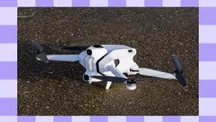 Side view of the white Antigravity A1 drone resting on a wet pebble surface