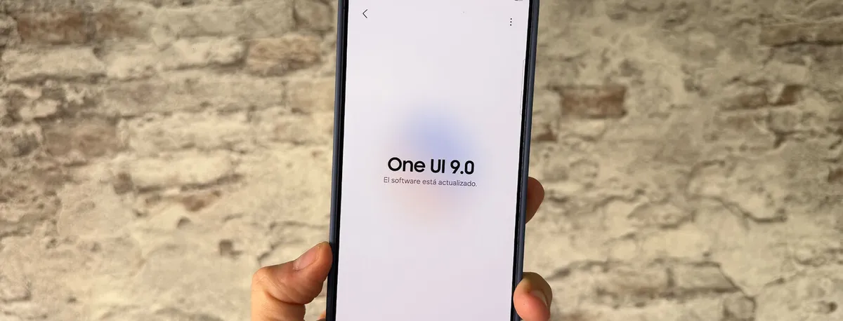 Un teléfono en mano muestra el aviso "One UI 9.0, el software está actualizado" frente a un muro de ladrillo