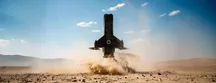 A Powerus Systems aircraft lifting off vertically over the desert, with a cloud of dust kicked up by its rotors