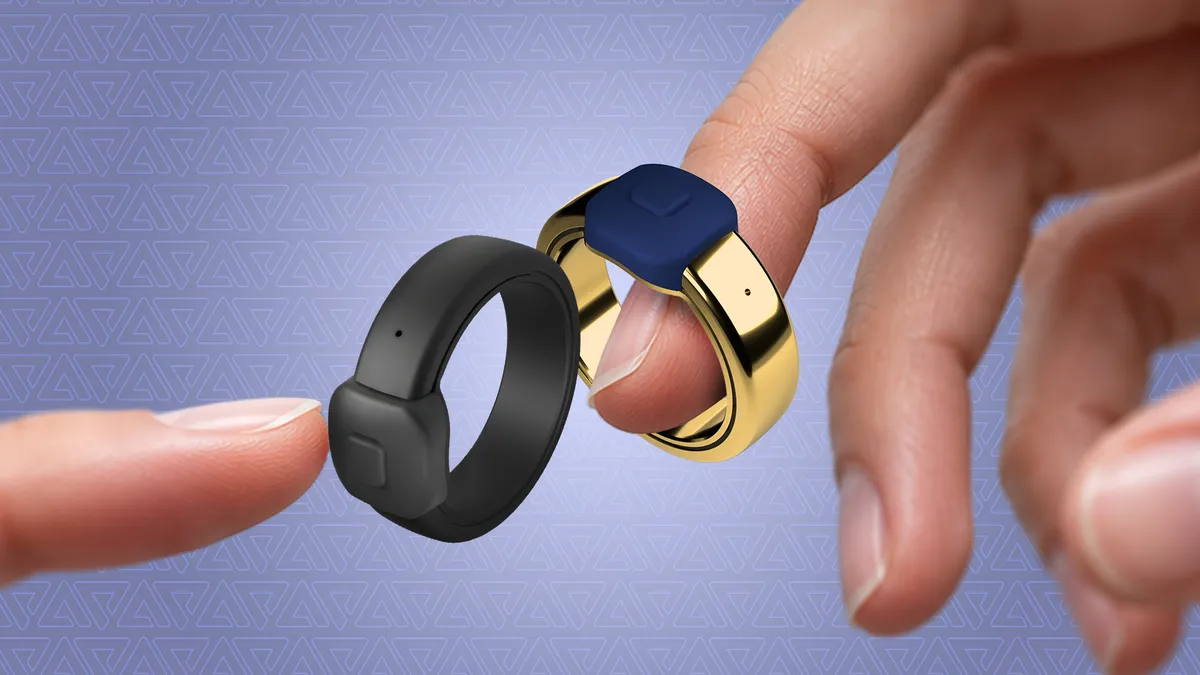 Two Pebble Index 01 rings held between fingers, one black and one gold with a blue button