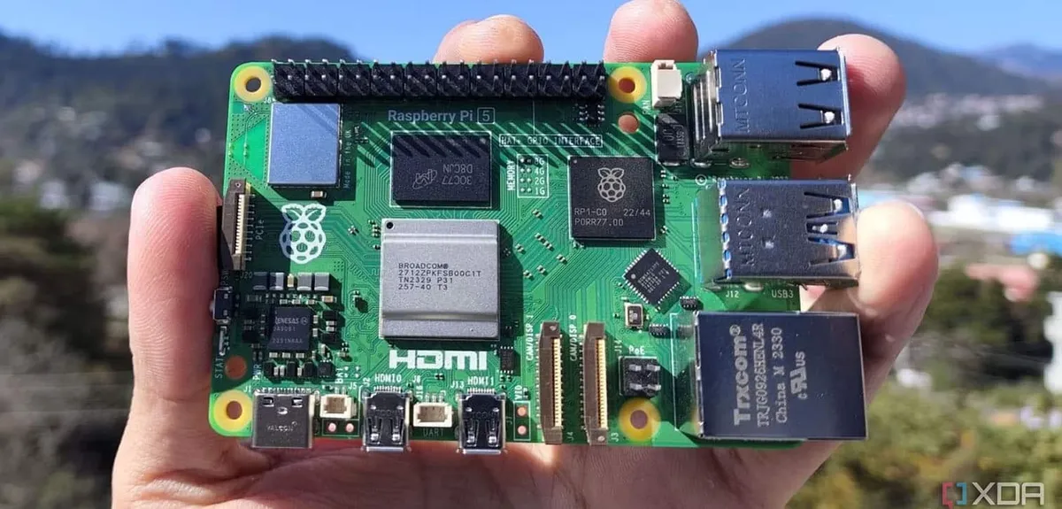 Una persona sostiene una placa Raspberry Pi 5 en la mano, con sus puertos USB, HDMI y Ethernet visibles sobre un fondo exterior desenfocado.