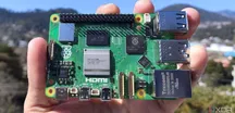 A person holding a Raspberry Pi 5 board in one hand, with its USB, HDMI and Ethernet ports visible against a blurred outdoor background.