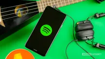 Teléfono con el logotipo de Spotify en pantalla sobre una superficie verde, junto a una guitarra y unos auriculares