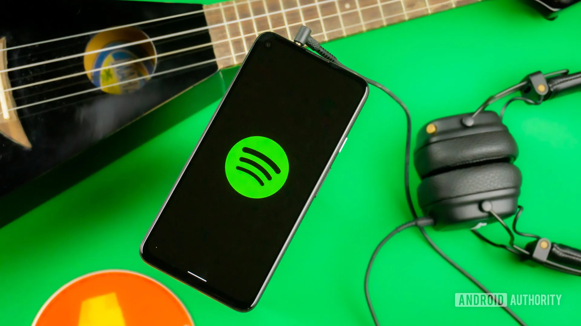 Teléfono con el logotipo de Spotify en pantalla sobre una superficie verde, junto a una guitarra y unos auriculares