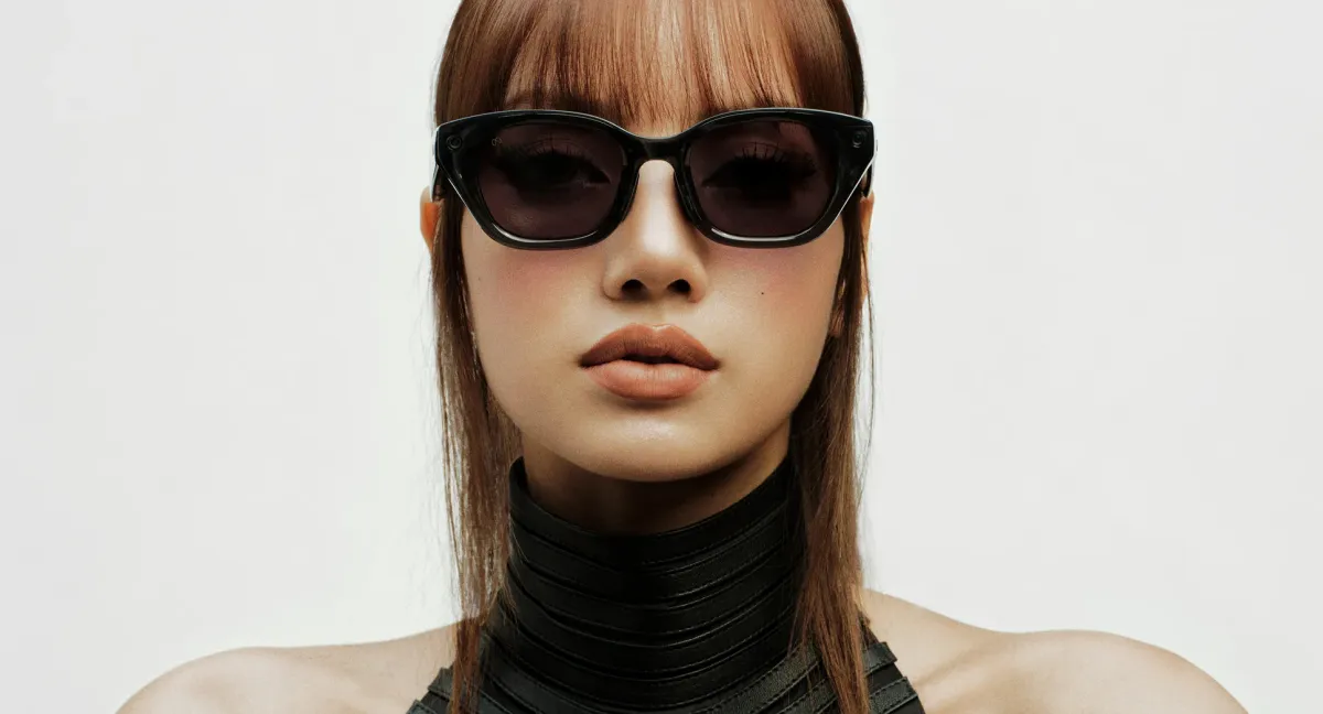 Portrait of a person wearing thick-framed black sunglasses against a white background