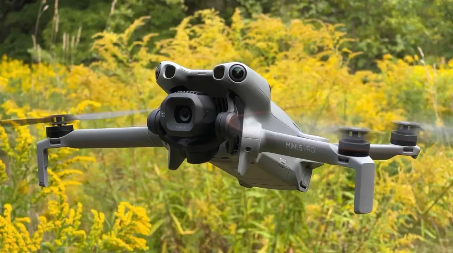 El DJI Mini 5 Pro volando de frente sobre flores, con el LiDAR y los sensores frontales apuntando a la cámara
