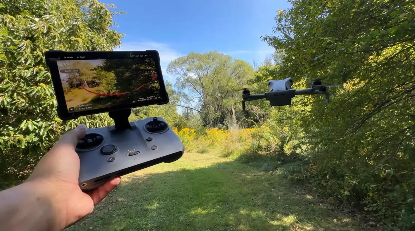 Un piloto sostiene un mando DJI RC 2 con la señal de cámara en vivo mientras el Mini 5 Pro vuela sobre un sendero