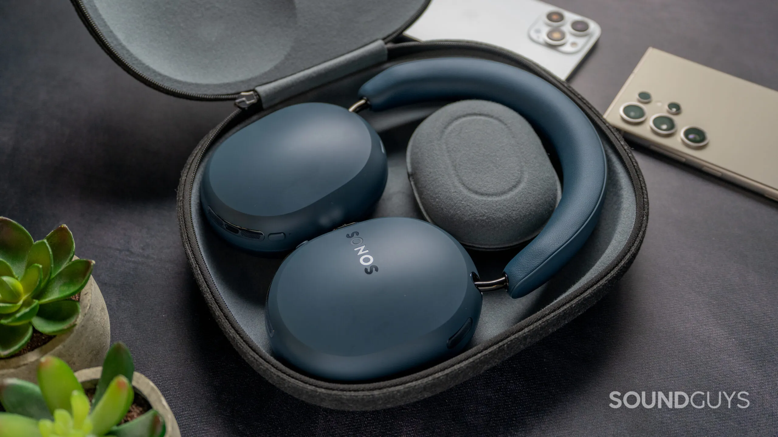 Auriculares Sonos Ace Ultra dentro de su estuche, junto a plantas y un teléfono