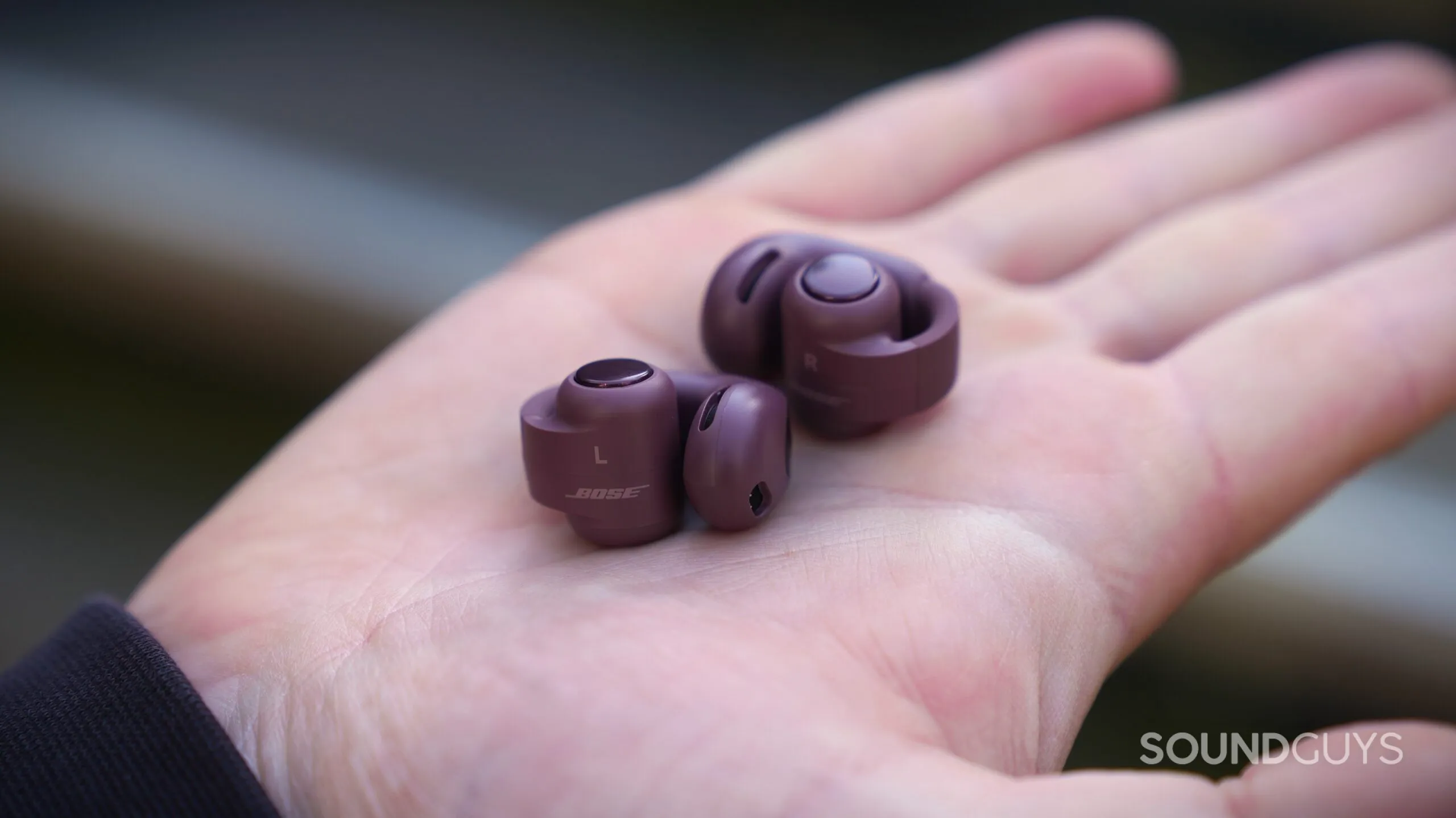 Auricular Bose Ultra Open 2 en la palma de la mano, con sus marcas de izquierda y derecha y el botón de control