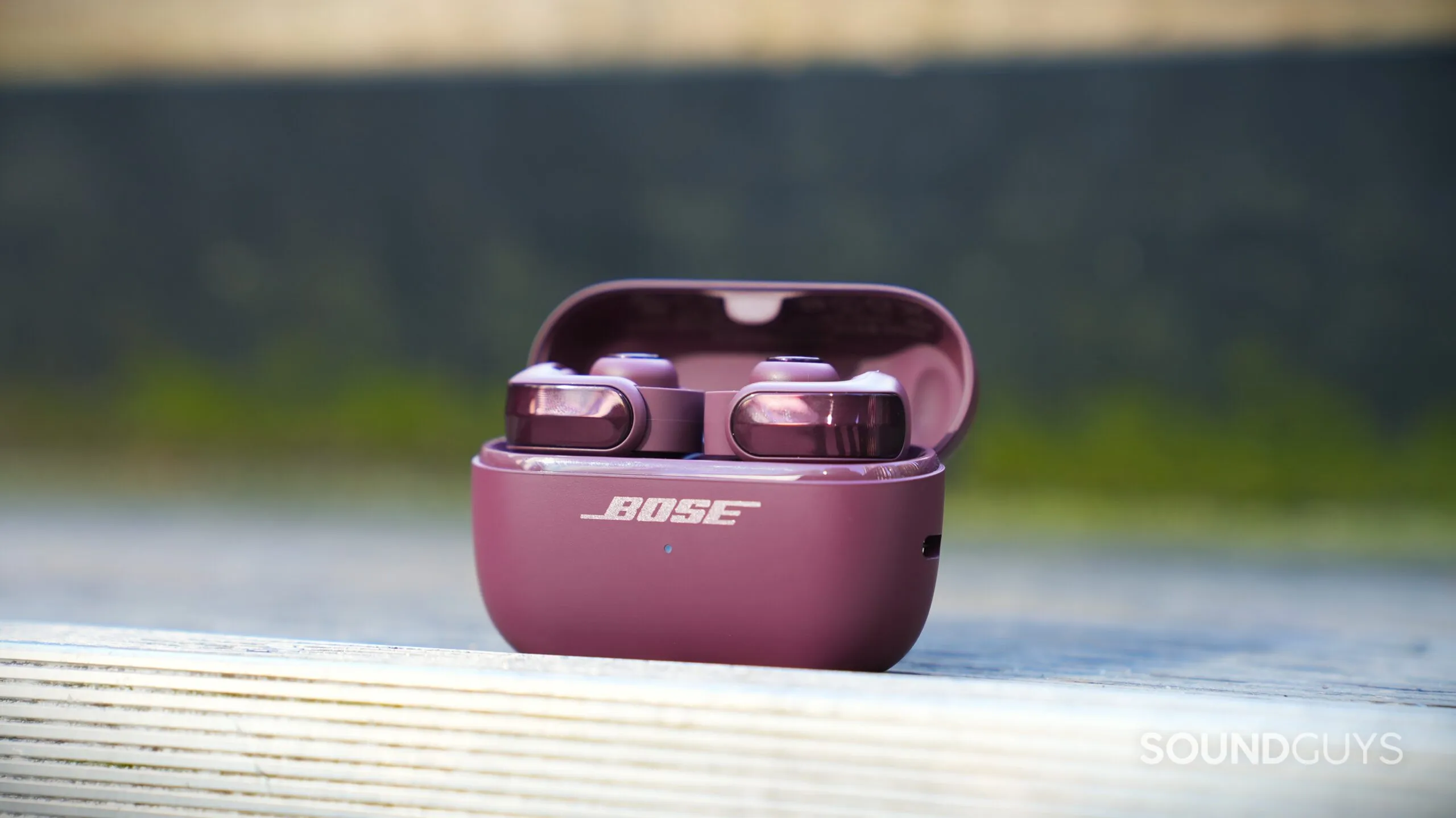 Auriculares Bose Ultra Open 2 en su estuche abierto sobre una barandilla de madera en el exterior