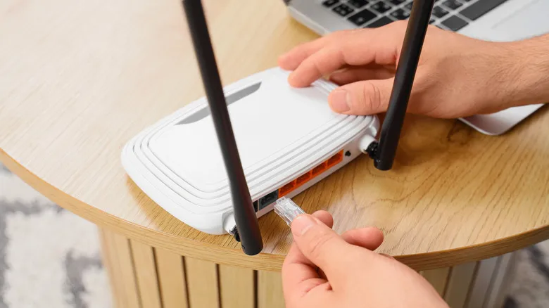 Persona que conecta un cable Ethernet a un router inalámbrico junto a un portátil