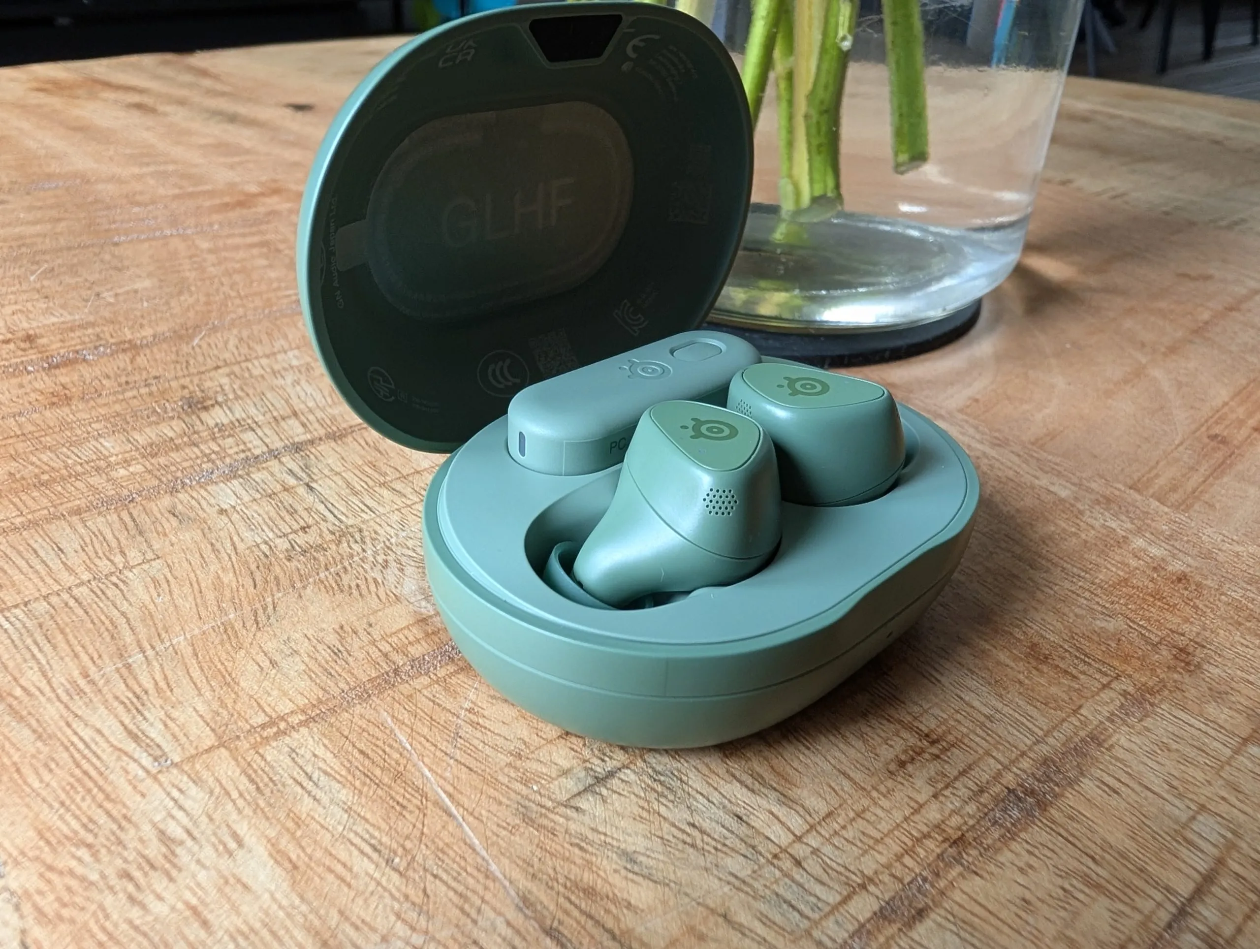 Auriculares Arctis GameBuds en verde junto a su estuche de carga y el adaptador USB-C