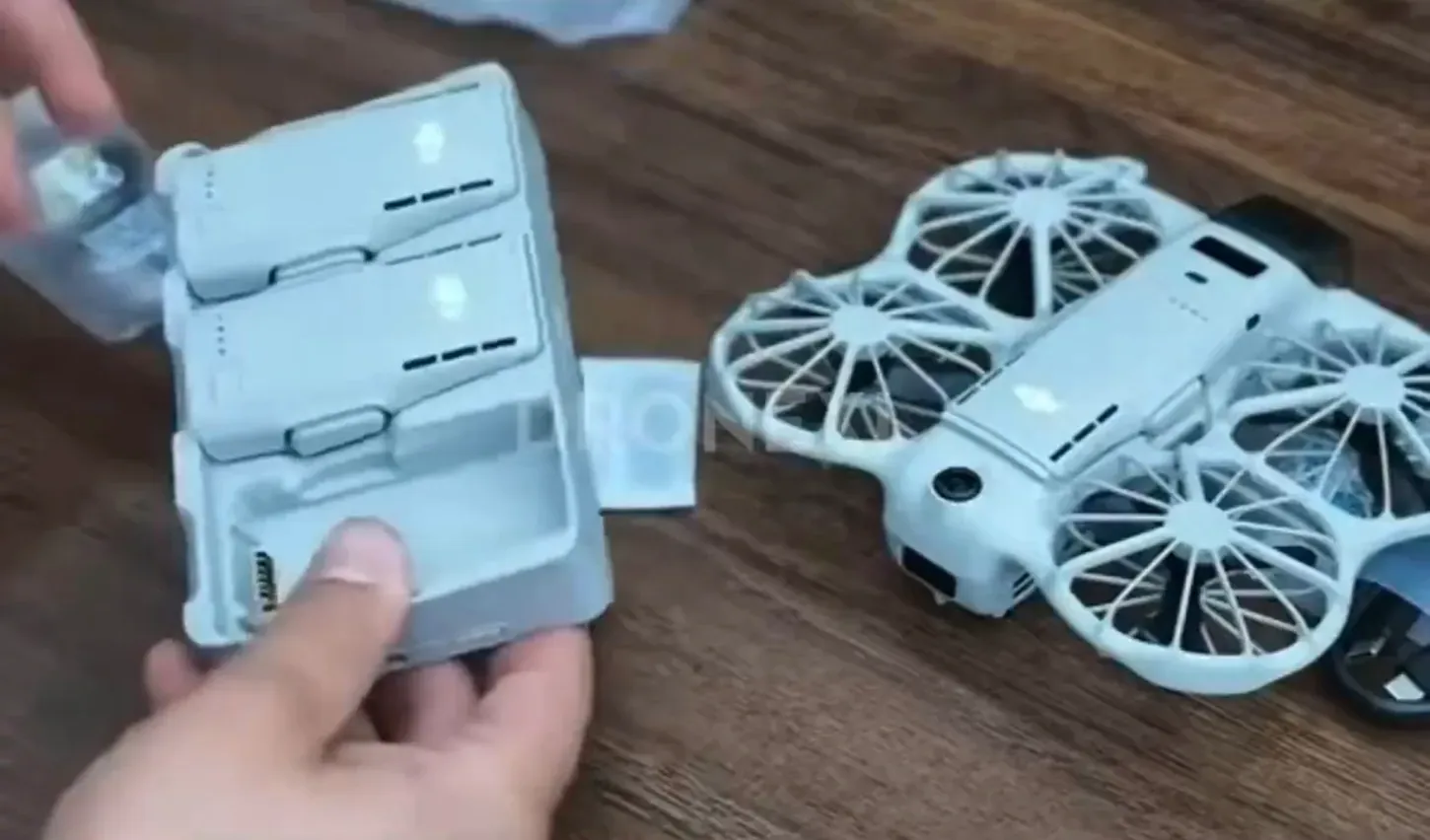 Hub de carga del DJI Neo 3 con dos baterías de vuelo, cada una con ranuras negras en su cara superior, junto al dron con jaulas en las hélices