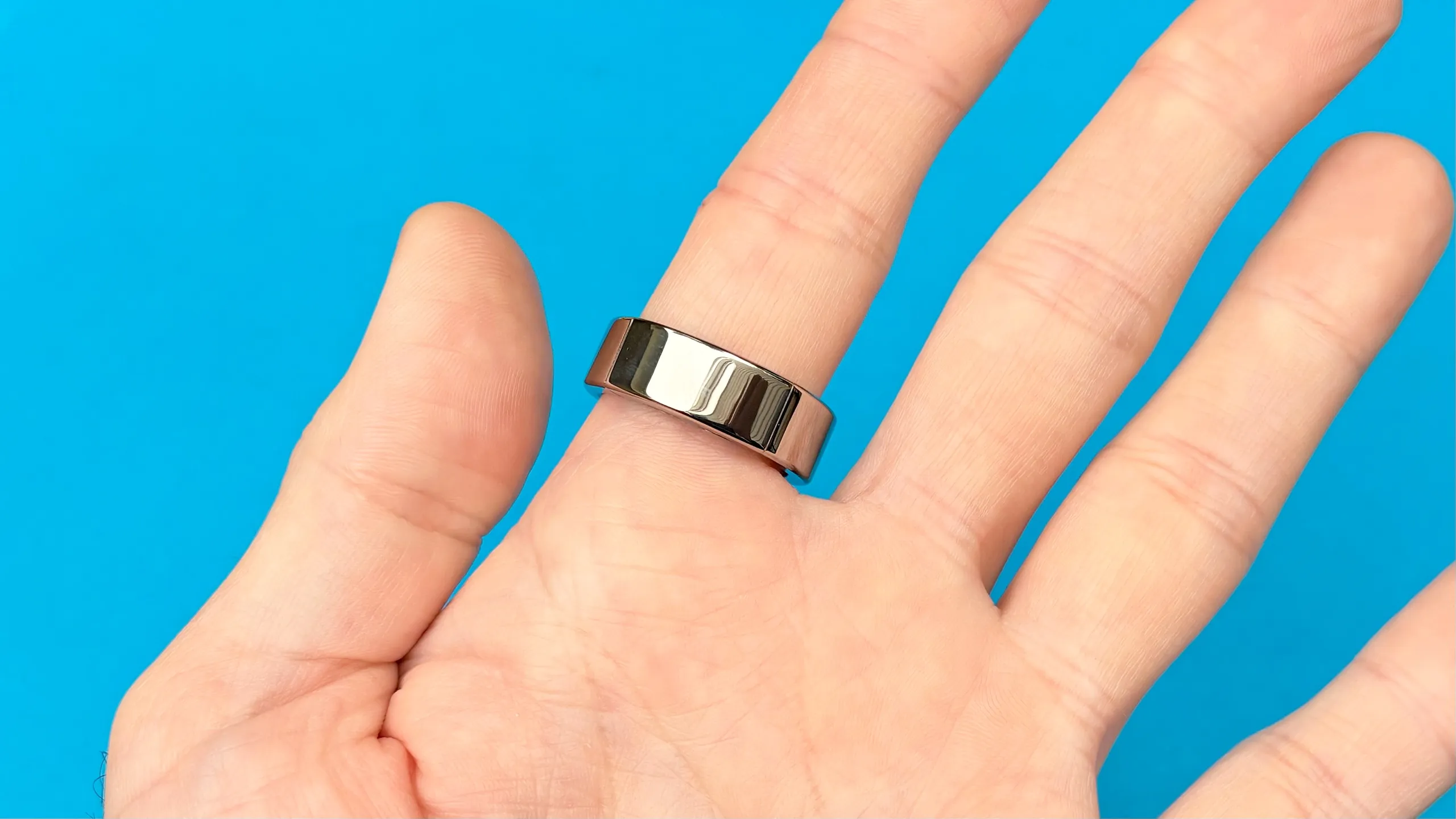 Ultrahuman Ring Pro plateado colocado en un dedo sobre un fondo azul