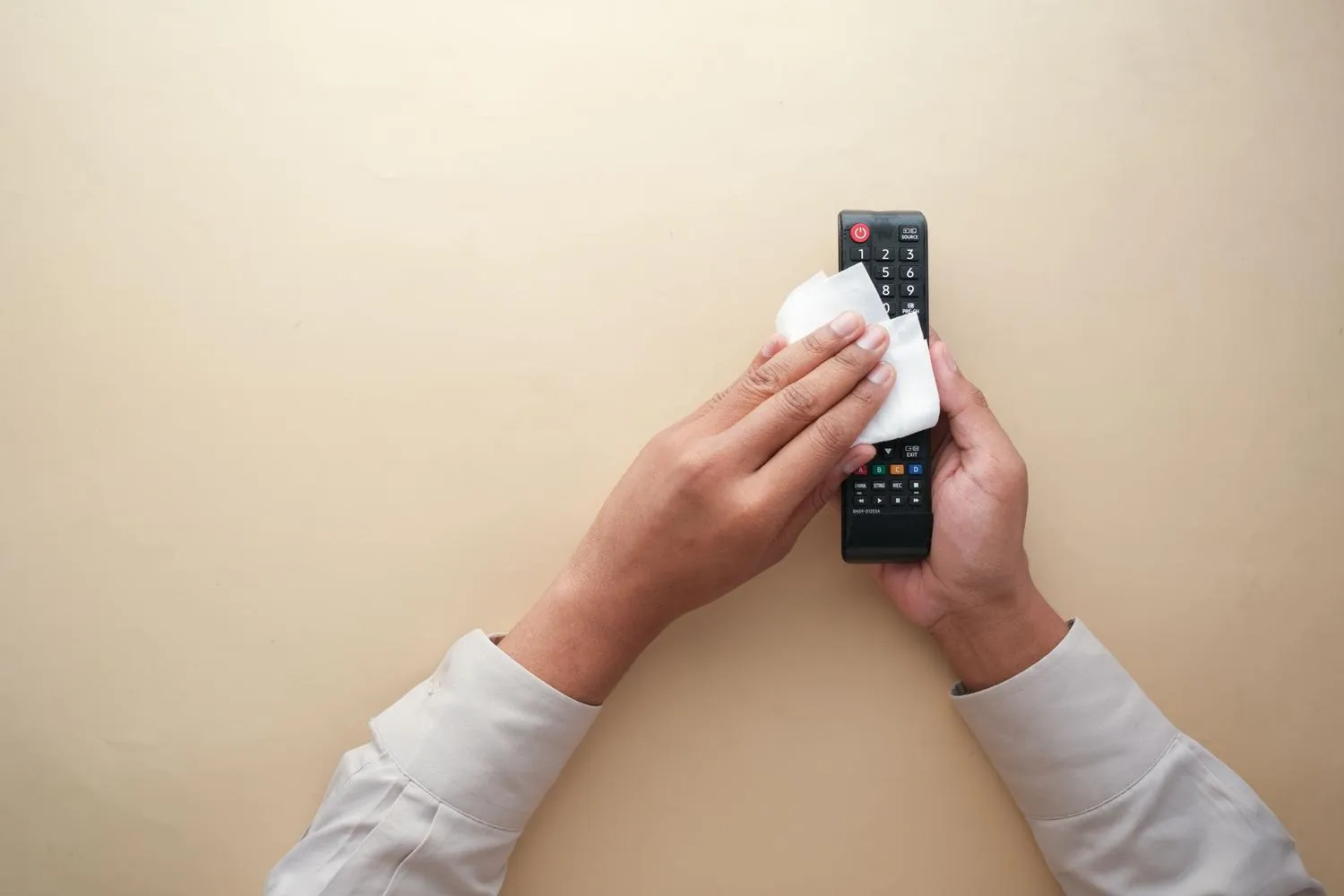 Hands cleaning a TV remote control with a cloth