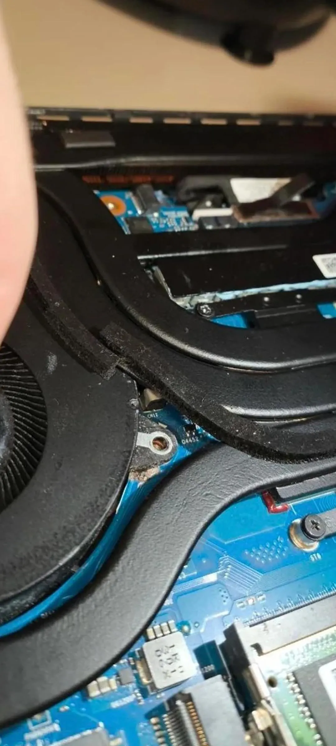 Detalle del interior de la ROG Strix G16 junto al ventilador, con la zona del anclaje y la cinta aplicada sobre la placa base