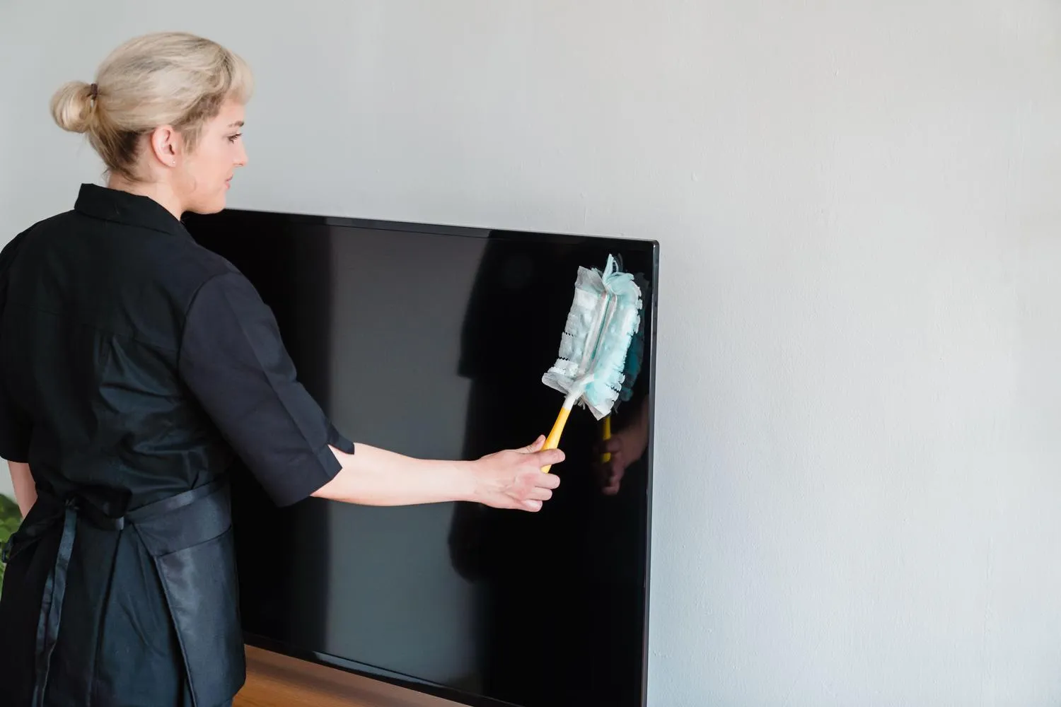 Person removing surface dust from a flat screen with a feather duster