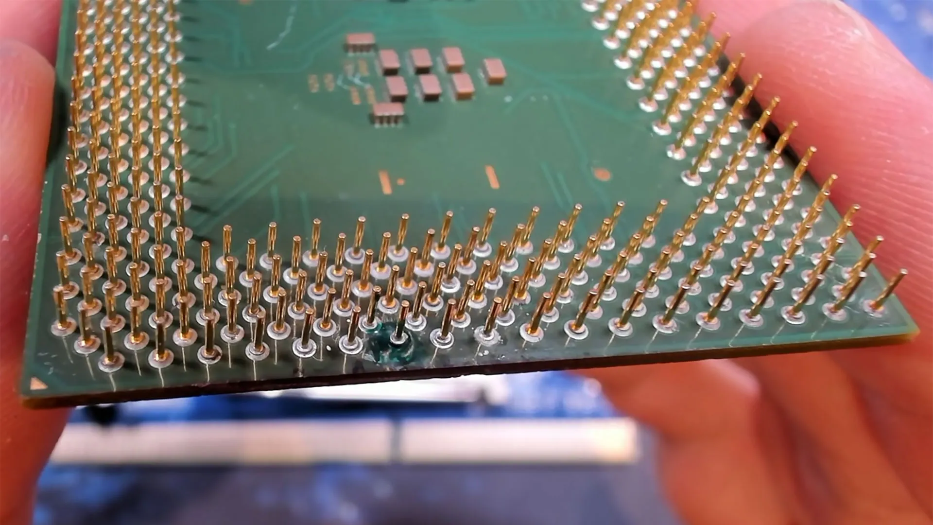 Vista inferior del Celeron 1200 sostenido en la mano, con la zona reparada junto al resto de pines