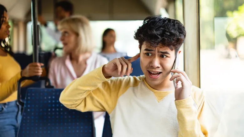 Joven en un autobús lleno de gente mientras atiende una llamada con el móvil