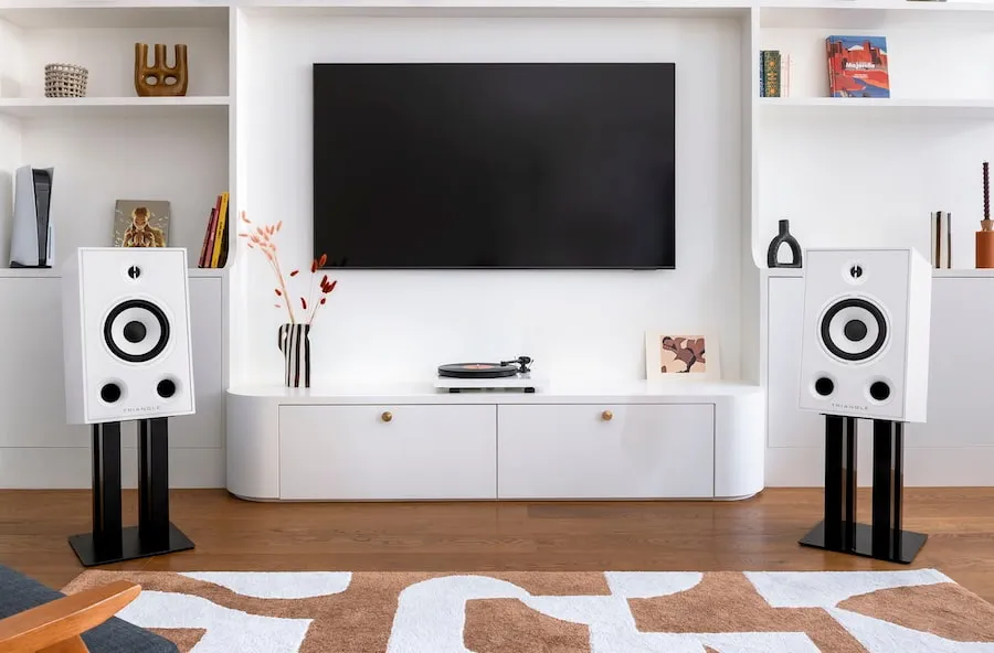 Two white Borea BR05 speakers on black stands on either side of a unit holding a television and turntable